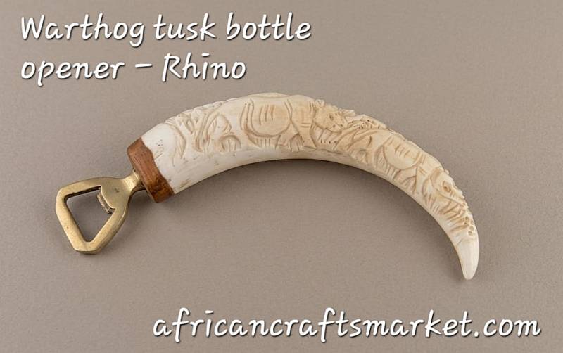 Hand-carved African warthog tusk bottle opener featuring a detailed relief carving of a rhinoceros along the natural curve of the tusk