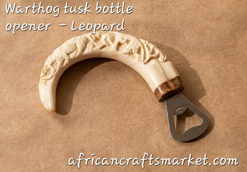 A genuine African warthog tusk bottle opener featuring a detailed, hand-carved 3D relief sculpture of a leopard along the natural curve of the ivory handle.