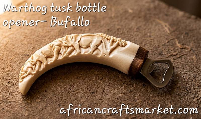A genuine African warthog tusk bottle opener featuring a detailed, hand-carved 3D relief sculpture of a Cape Buffalo head with a prominent horn boss along the ivory handle